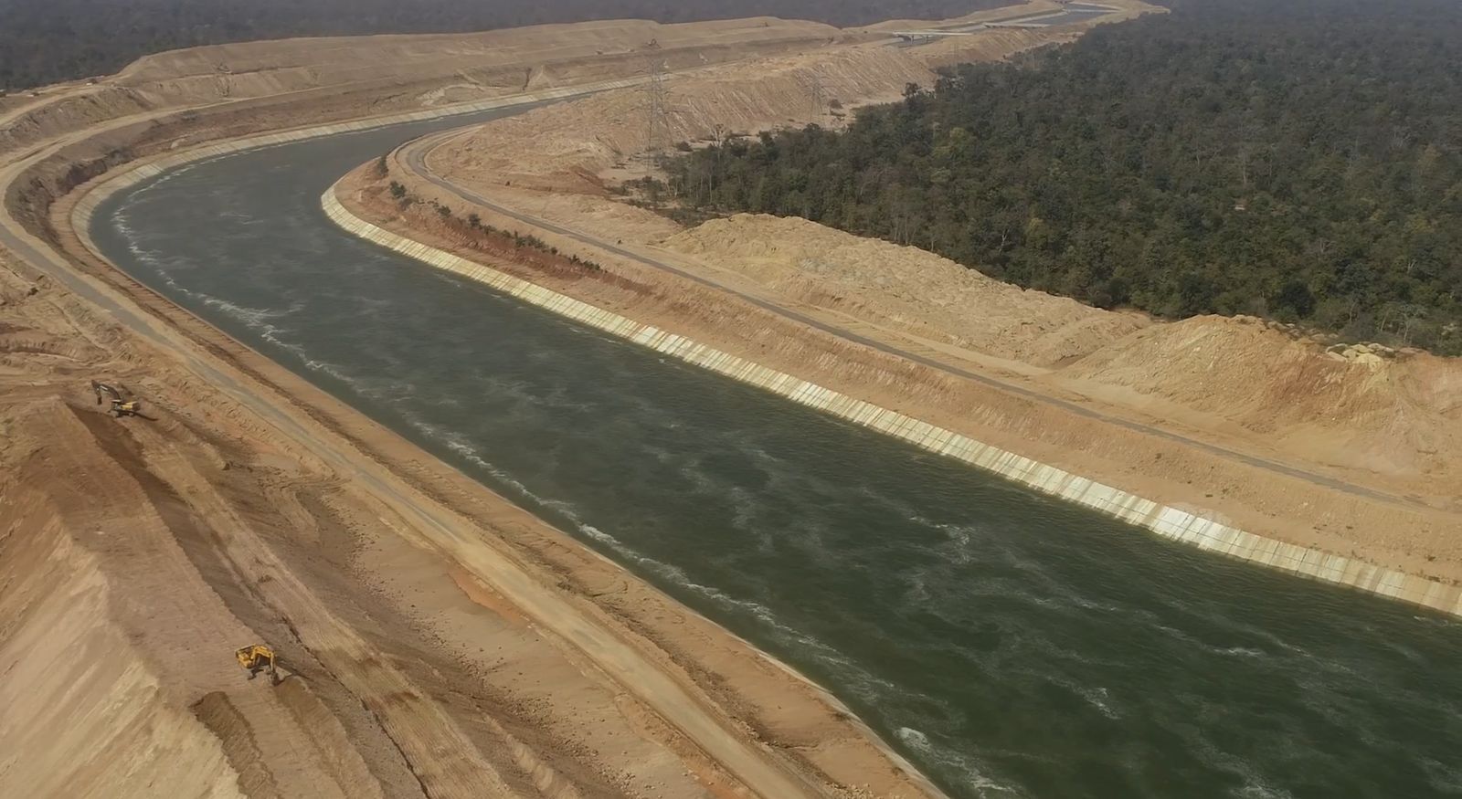 A wide lined canal carrying water through cut earth and scrub